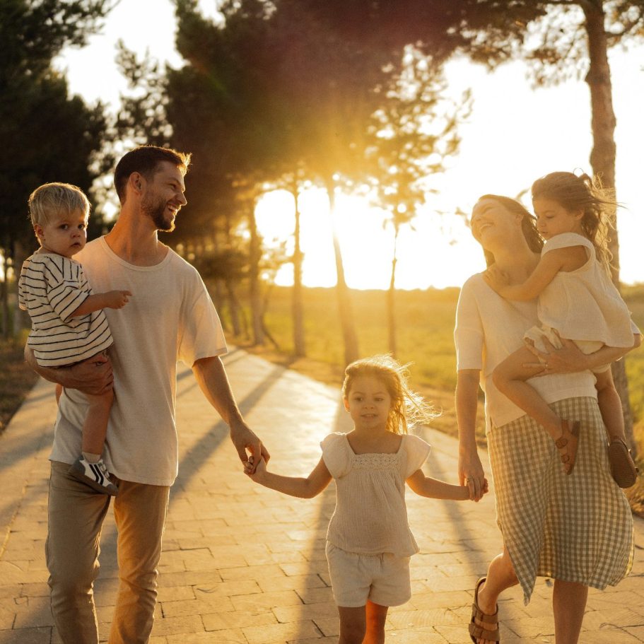 Willkommen in der Welt Familie spaziert zusammen bei Sonnenuntergang an einem Baum entlang.